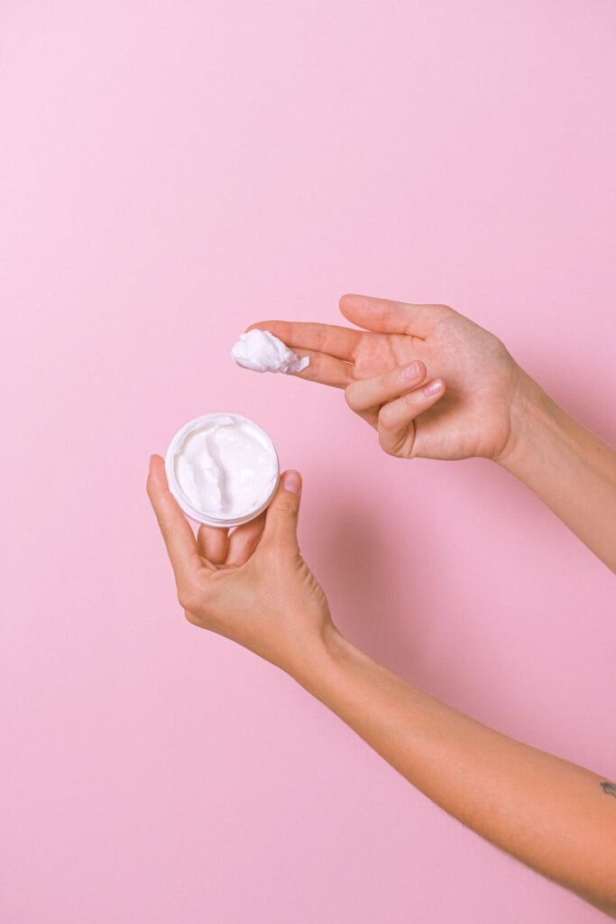 Unrecognizable person with can of moisturizing cosmetic cream for daily routine in hands on pink background in studio during procedure