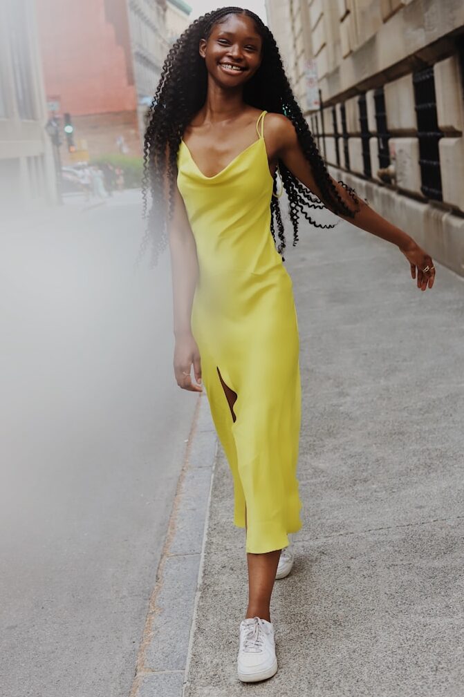 woman in yellow sleeveless dress standing on gray concrete pavement