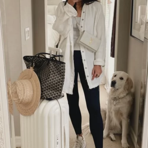 young woman standing in home posing with white luggage and bags getting ready for a trip while she's black leggings, chunky sneakers and a white linen button up
