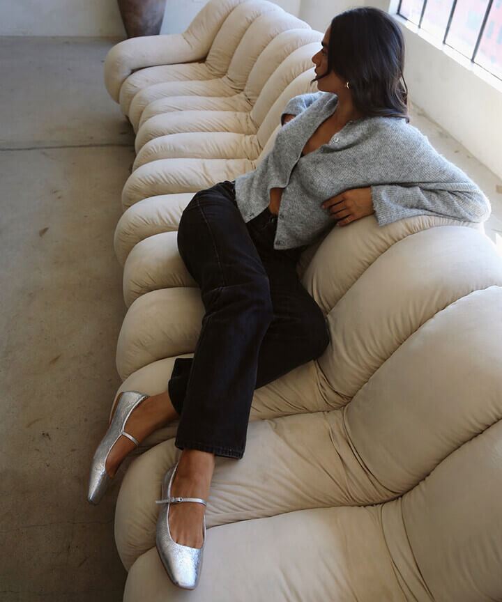 young woman on coach wearing metallic ballet flats