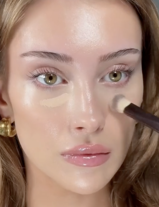 young woman applying concealer under eyes