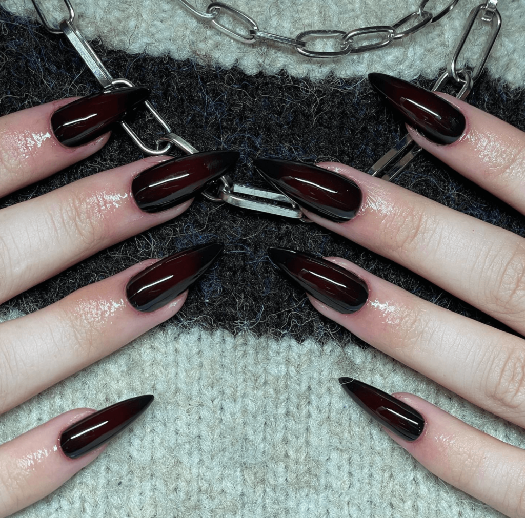 long nails painted in dark black red color against silver necklace