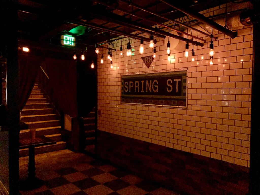 Mosiac wall sign of Spring St under string lights