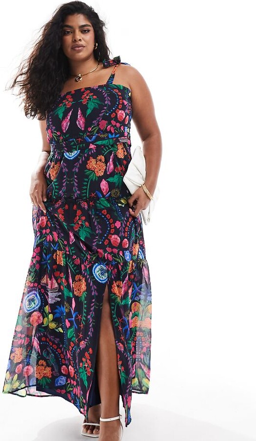 latina model wearing a colorful floral maxi dress against a black fabric