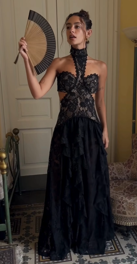 model wearing black lace gown with side cut out details holding a folding fan