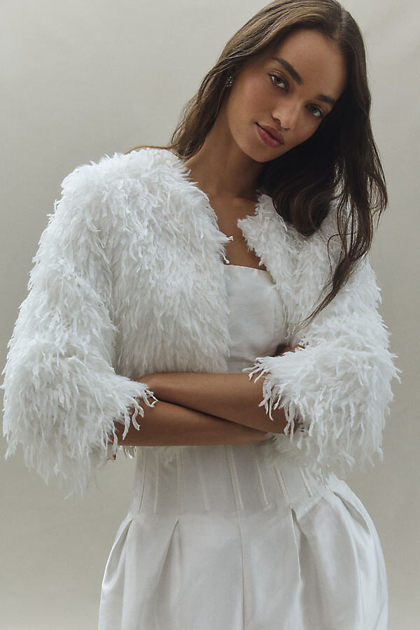 model wearing a shaggy cropped sleeve white cardigan over a fitted white bodice dress with her hands crossed