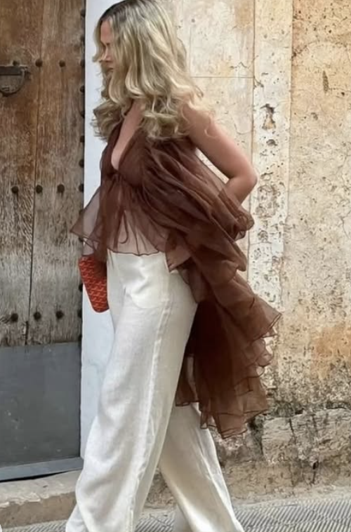 young blonde woman walking down the street side profile wearing a flowy high low chiffon ruffle brown halter top and cream stain pants