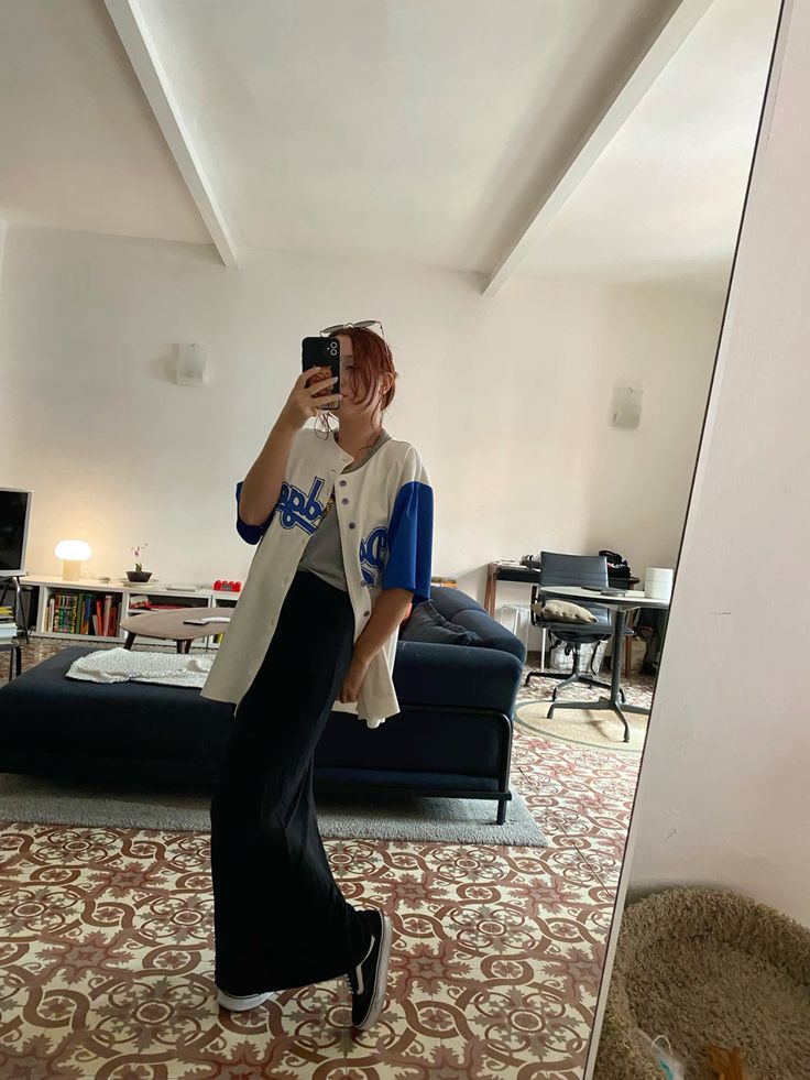 young woman taking mirror selfie wearing black satin maxi skirt styled with baseball jersey