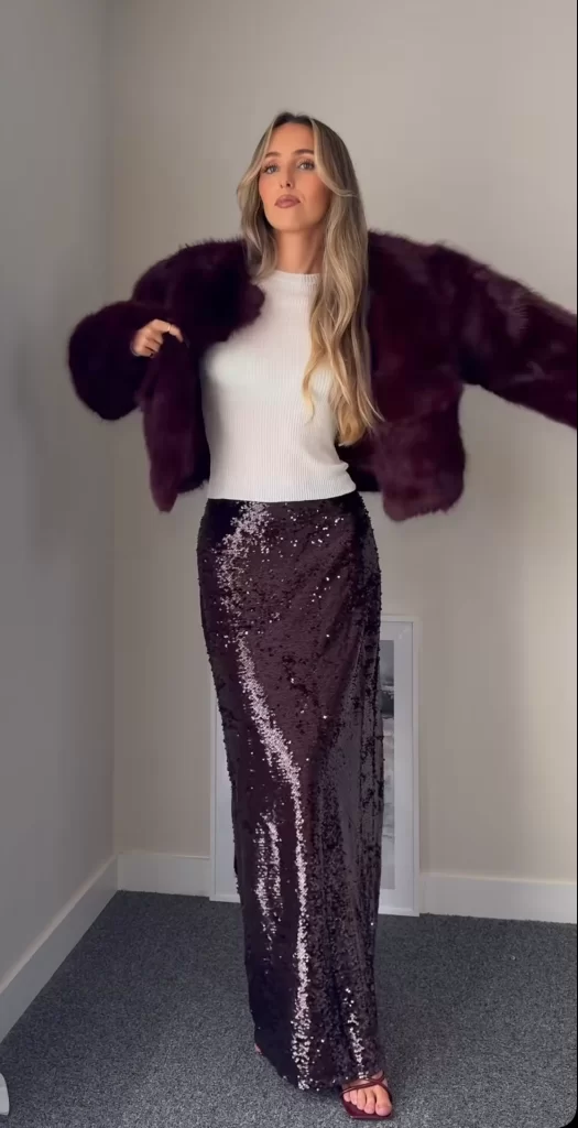 young woman wearing burgundy sequin maxi skirt, white top and burgundy faux fur coat