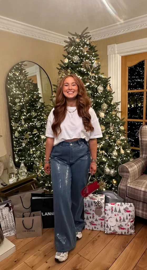 Young girl standing in front of Christmas tree wearing sparkly jeans and white tee