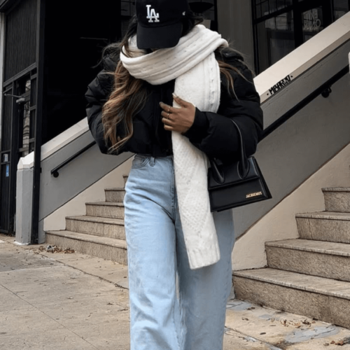 young woman with scarf wrapped around face wearing baseball cap leather jacket and jeans