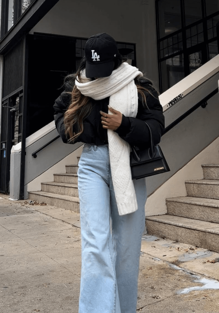 young woman with scarf wrapped around face wearing baseball cap leather jacket and jeans