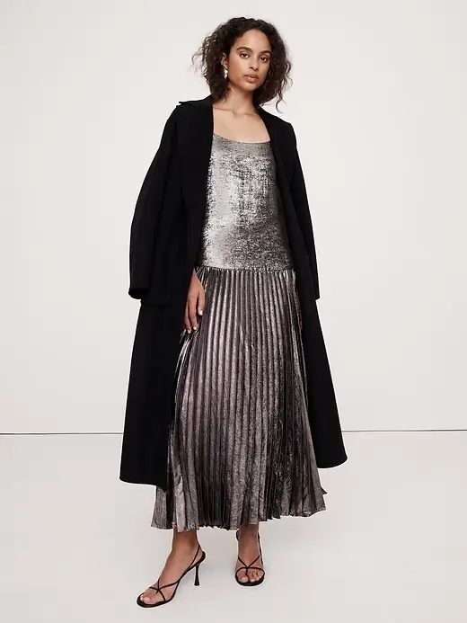 model wearing silver metallic pleated dress with long black coat over