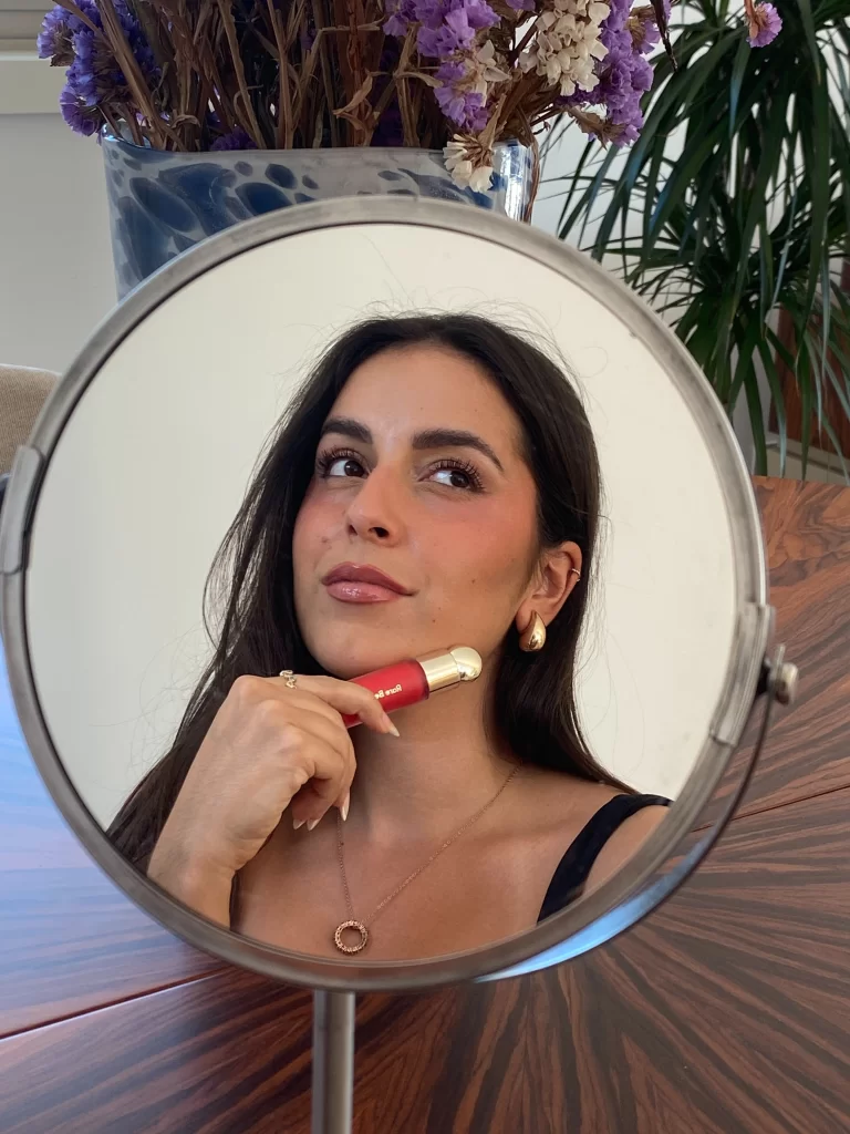 young woman in small mirror holding cream makeup