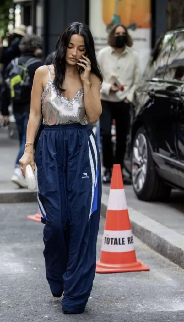 young woman walking down street wearing silver sequin cami and navy baggy track pants