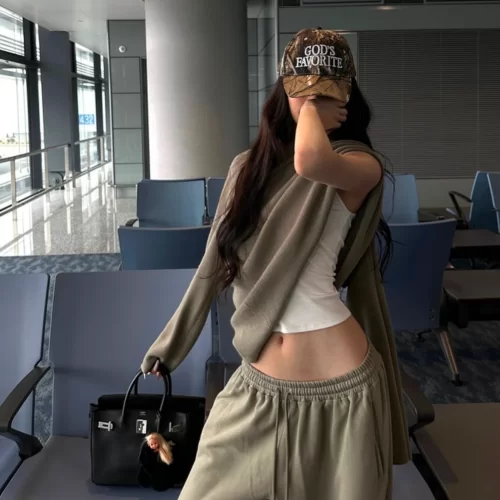 young woman posing in airport covering face but lift up sweatshirt to reveal white fitted tank underneath