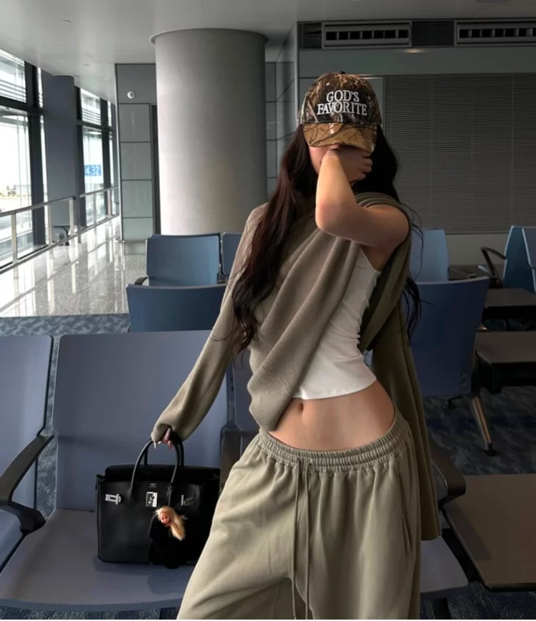 young woman posing in airport covering face but lift up sweatshirt to reveal white fitted tank underneath