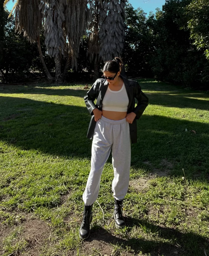 Young woman standing in park wearing grey sweats outfit with black leather blazer and black boots