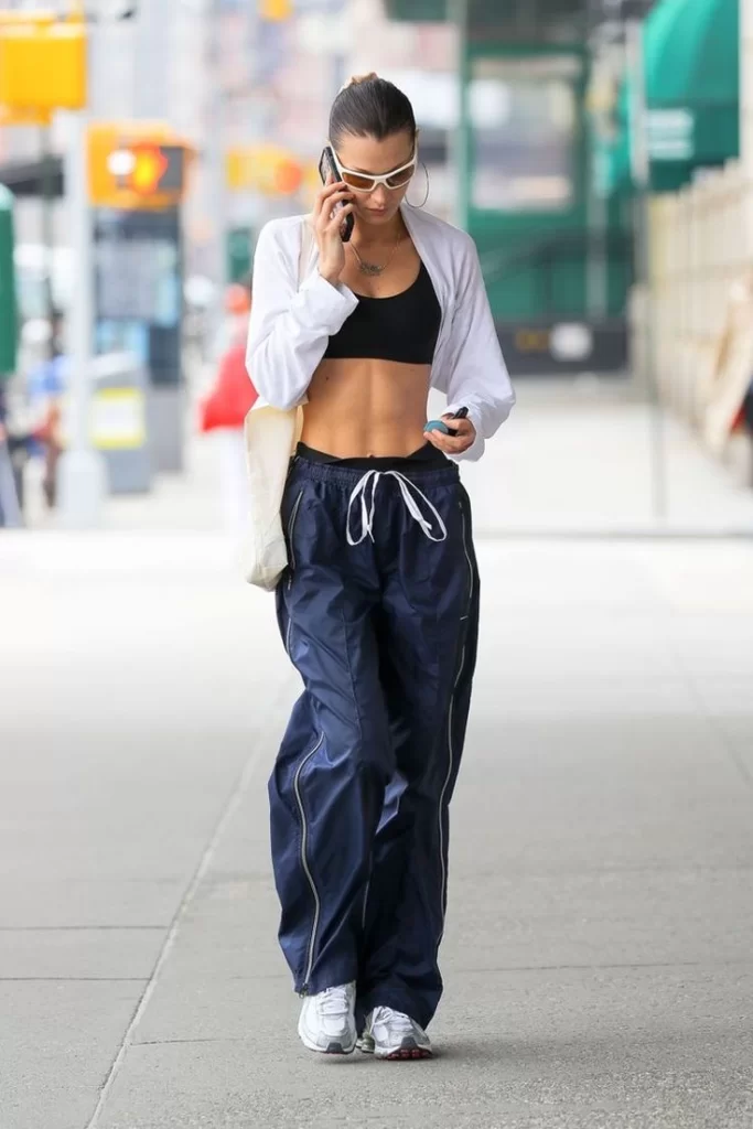 Bella Hadid walking down street wearing relaxed sweatpants outfit with bra top and button down shirt