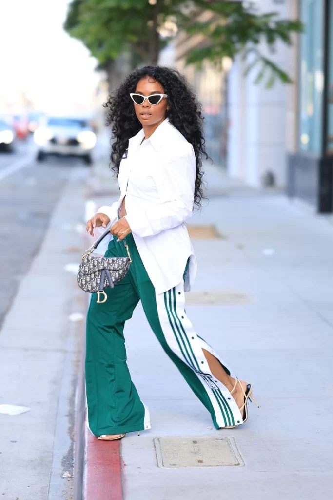 African American woman crossing the street wearing luxe sporty outfit with green track pants and white button down with heels