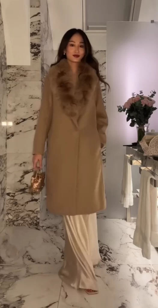 young asian woman wearing metallic slip dress and long camel color coat over