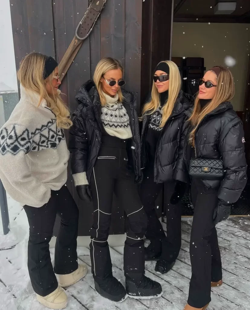 group of four women posing in black and white ski outfits while its snowing