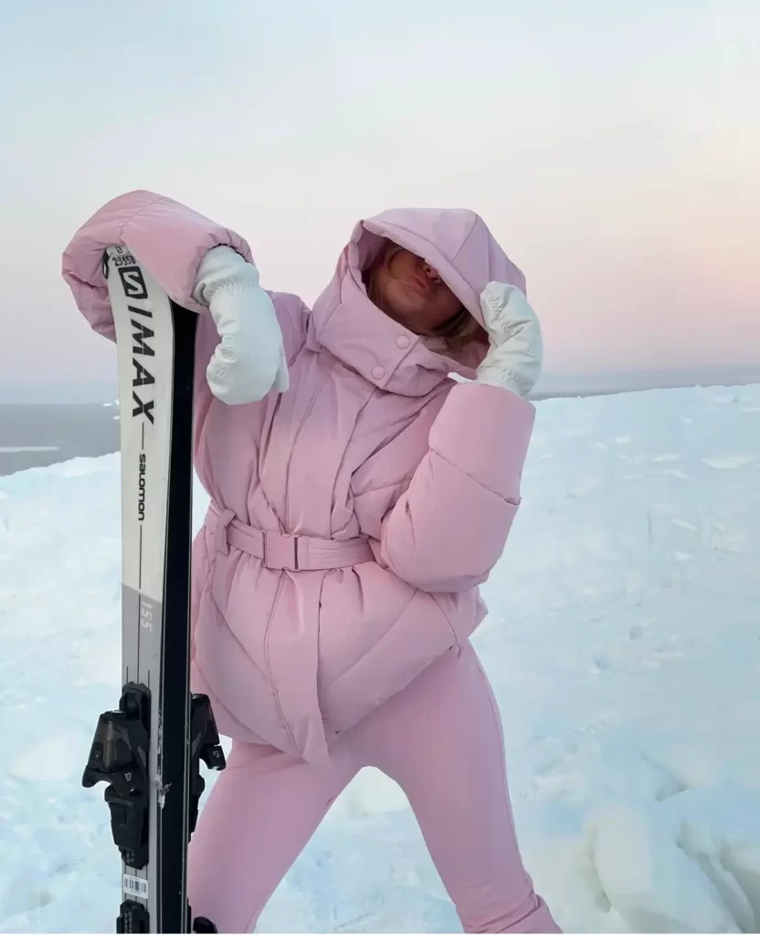 woman posing with skis in light pink ski outfit