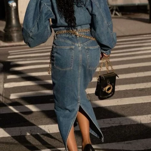 woman walking away down crosswalk face backing wearing long sleeve denim maxi dress with a chain belt and black heels