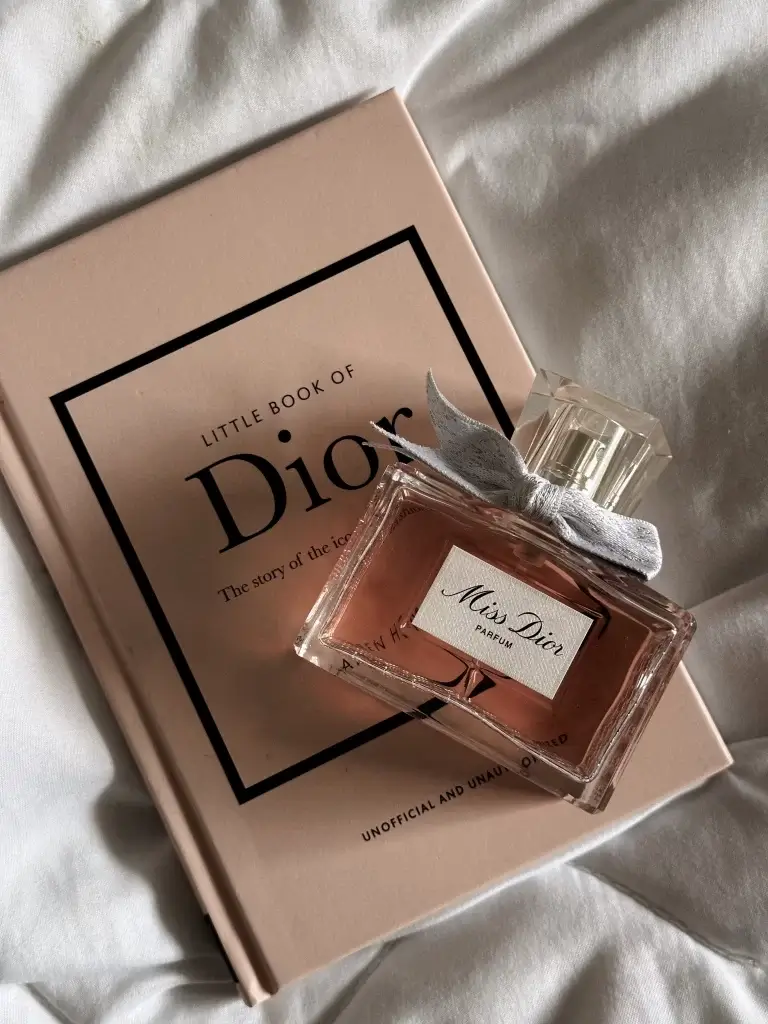 stylized shot of Miss Dior perfume bottle against a coordinated pink dior book on a bed linen