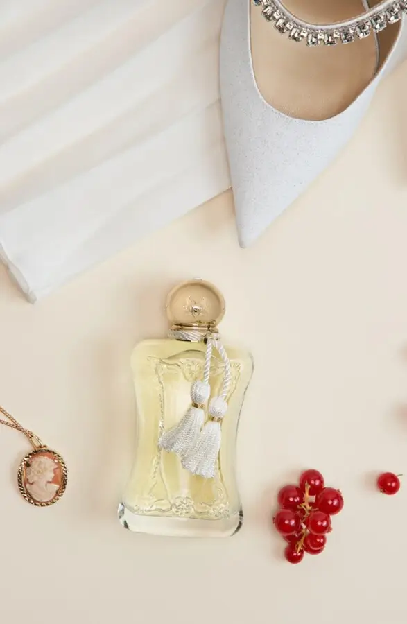 editorial shot of a luxury perfume bottle with red berries and a white bridal shoe