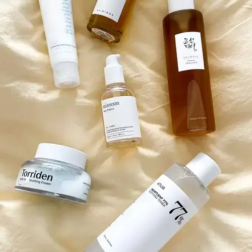 overhead shot of different Korean skincare serums laid out on satin fabric