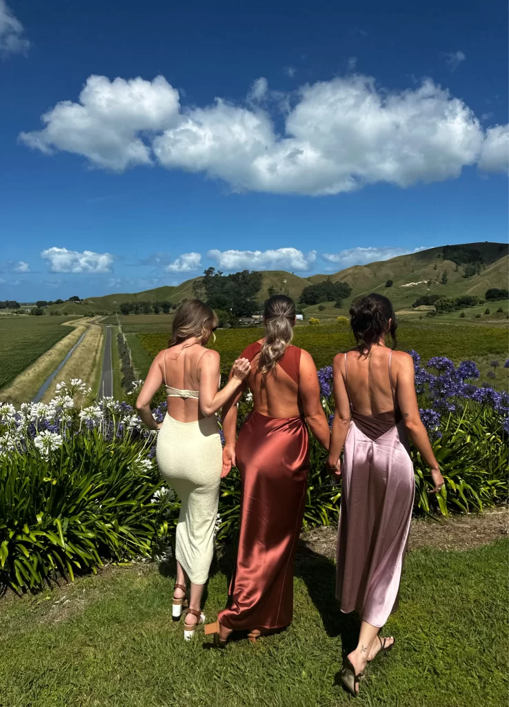 group of three woman posing with back towards camera against a hilly scene wearing different satin dresses
