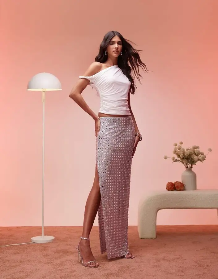 model wearing Oh Polly embellished maxi skirt in silver with an asymmetrical white tank top against a light pink background