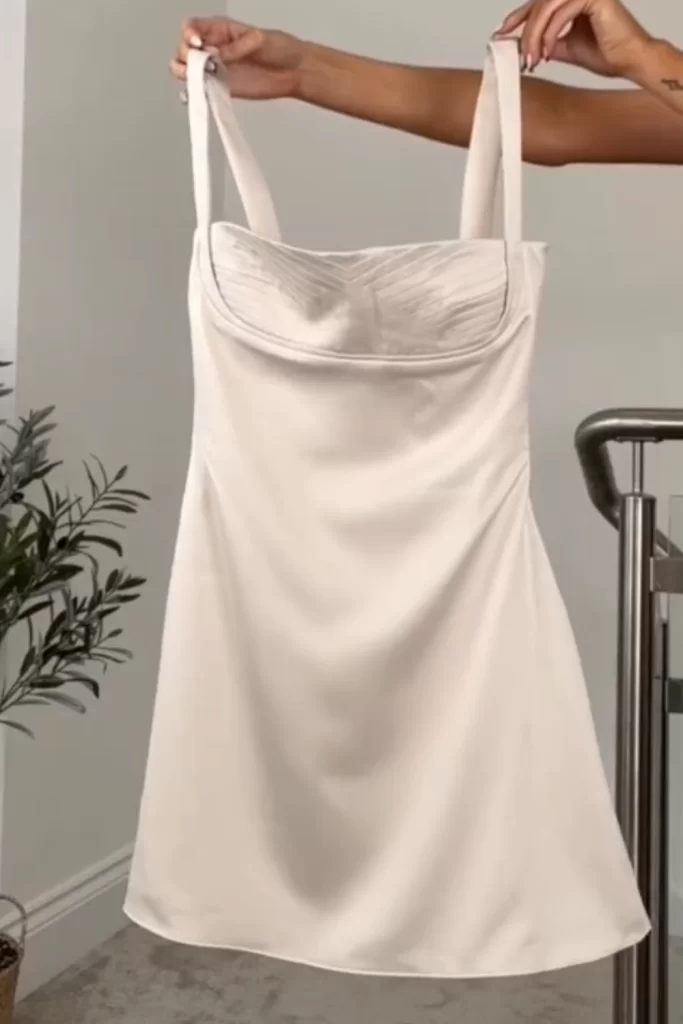 Close up of a white satin mini dress being held up against wall