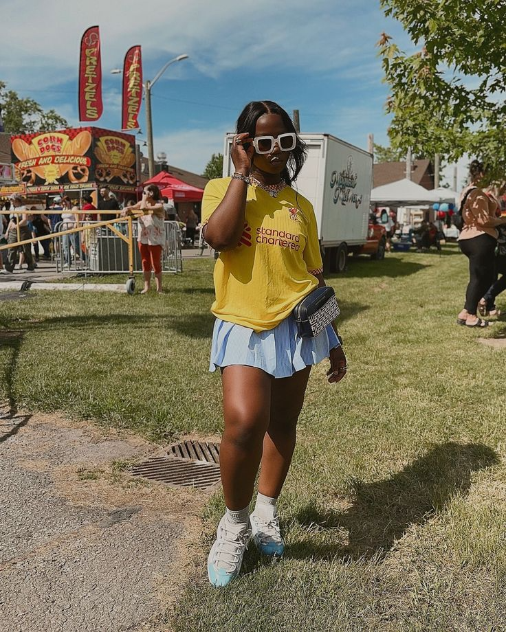 young black woman wearing a pleated mini skirt blue paired with a bright yellow t-shirt standing in an amusement park