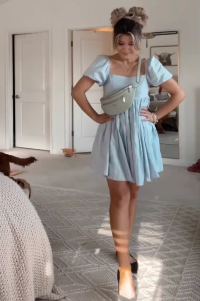 woman posing in bedroom sharing her amusement park outfit which is a blue puff sleeve mini dress, black ballet flats and space buns hairstyle