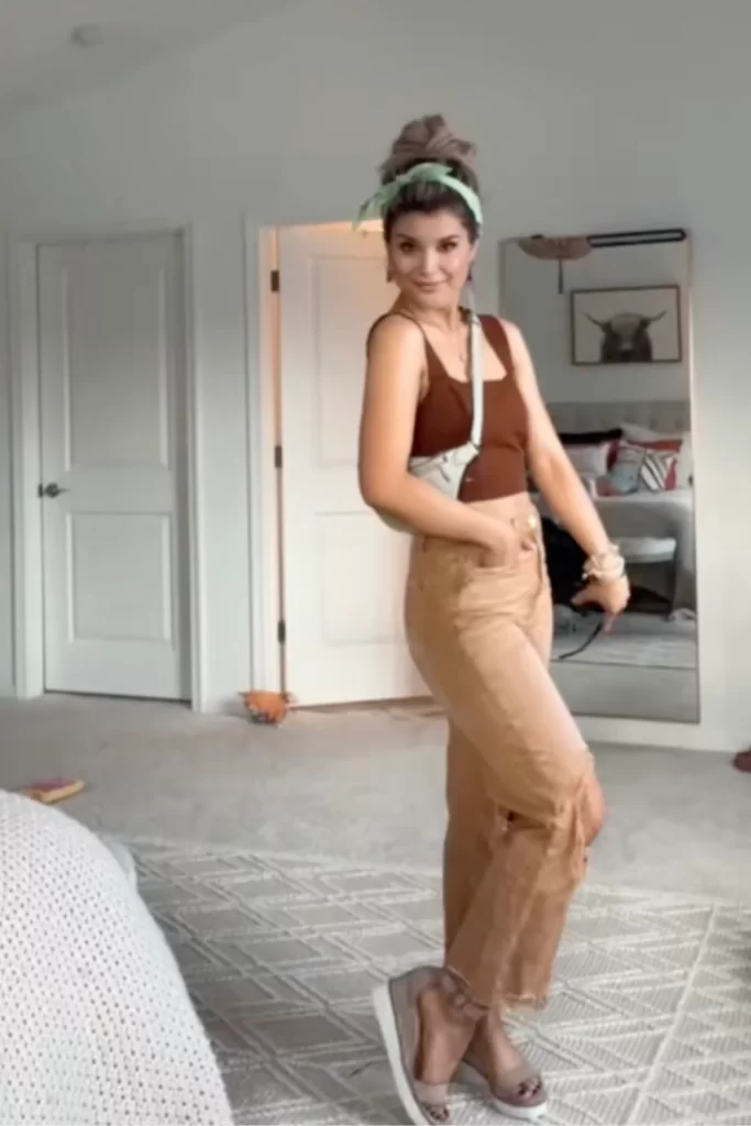 influencer standing in bedroom showing off her amusement park outfit ideas styling a brown tone wide leg jean with a darker brown tank top