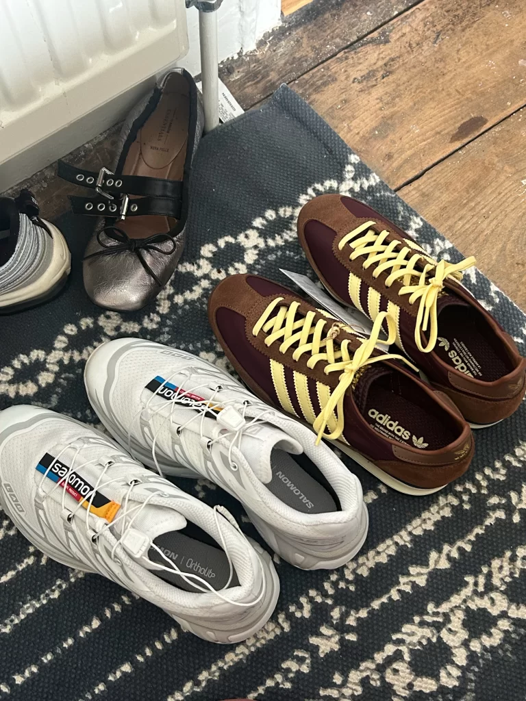 photo of different casual shoe options laid on rug including white solomons, brown adidas and silver mary janes