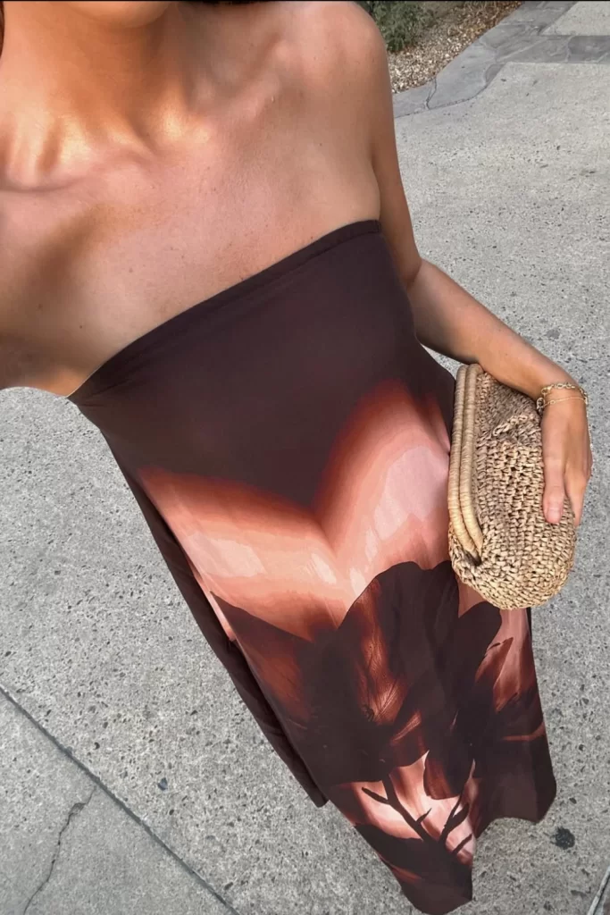 cropped photo of woman wearing strapless printed maxi dress with a woven clutch