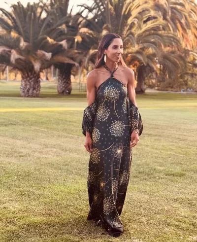 fall boho wedding guest outfit idea with black dress and gold graphic detailing with off the shoulder balloon sleeves on woman in field