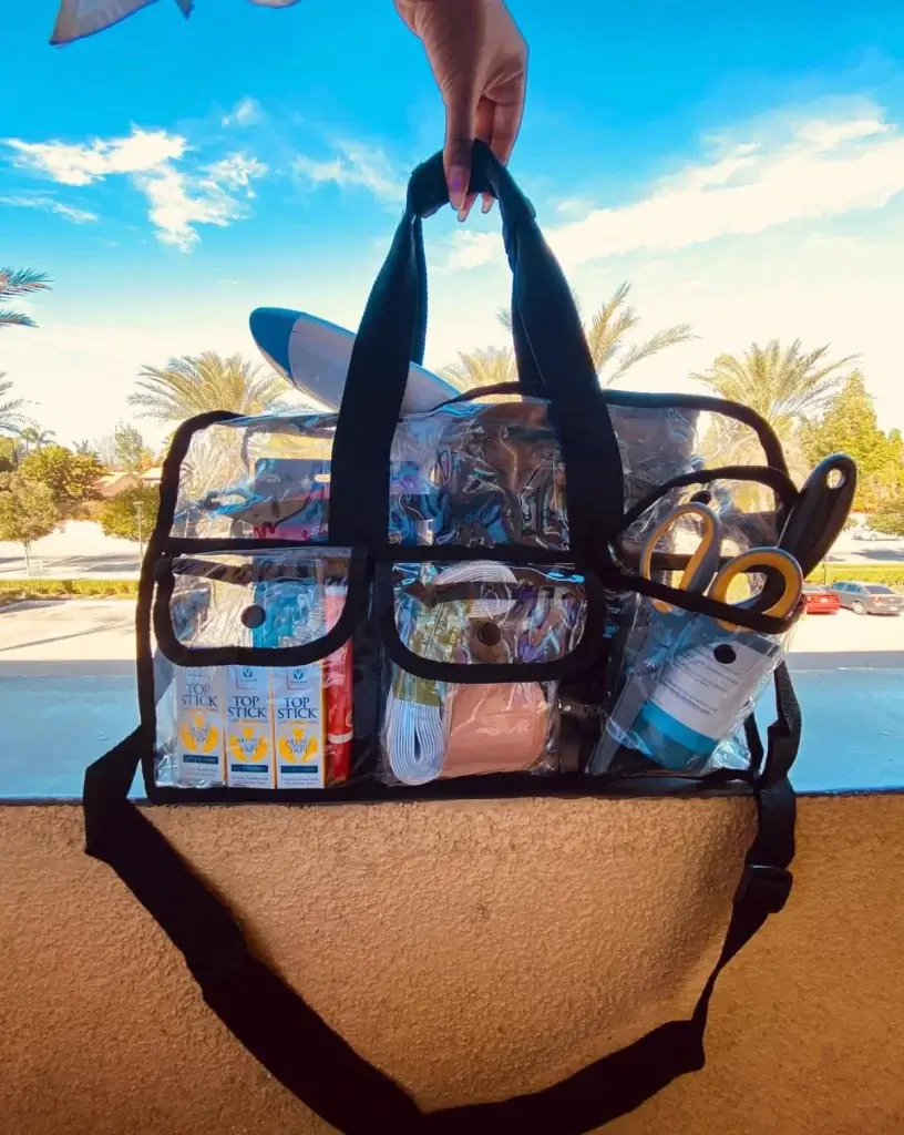 close up of clear stylist kit bag where you can see wardrobe essentials like scissor, double sided tape, lint roller and other necessities