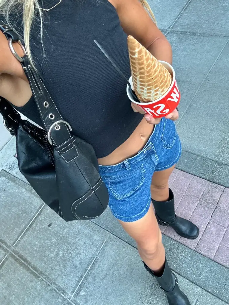 cropped photo of woman wearing black boots in summer with denim shorts and black tank while eating ice cream