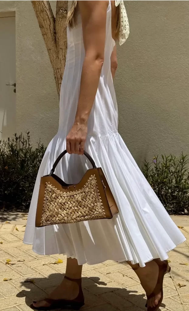 Cropped photo of woman wearing lightweight white maxi dress, straw tote and brown leather kitten heeled sandals as a summer outfit