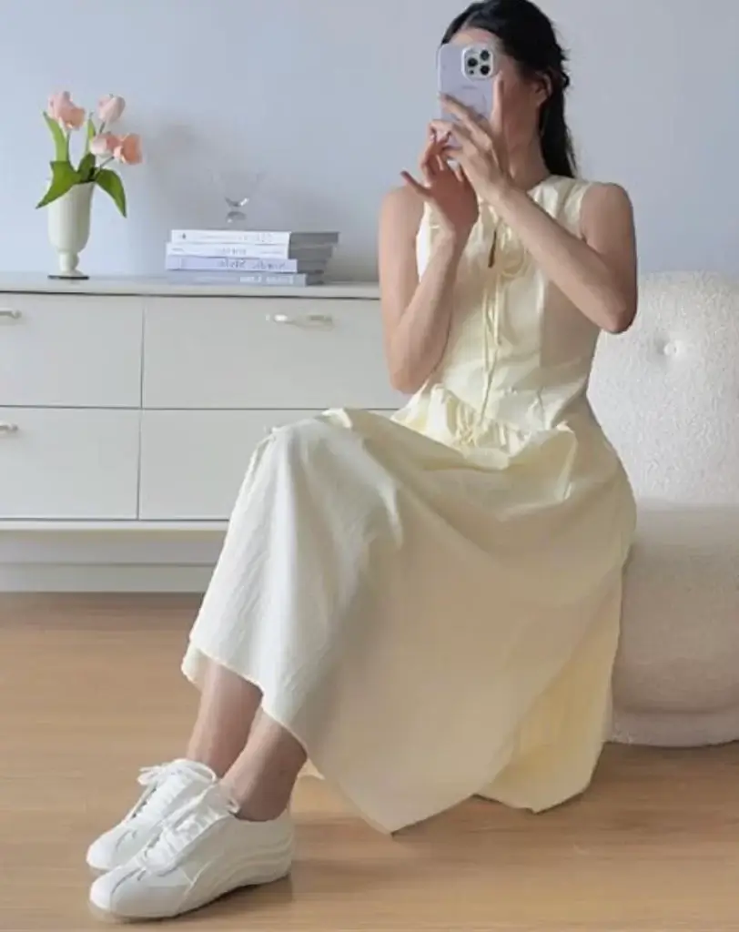 woman sitting on chair wearing white flowy dress and white sneakers