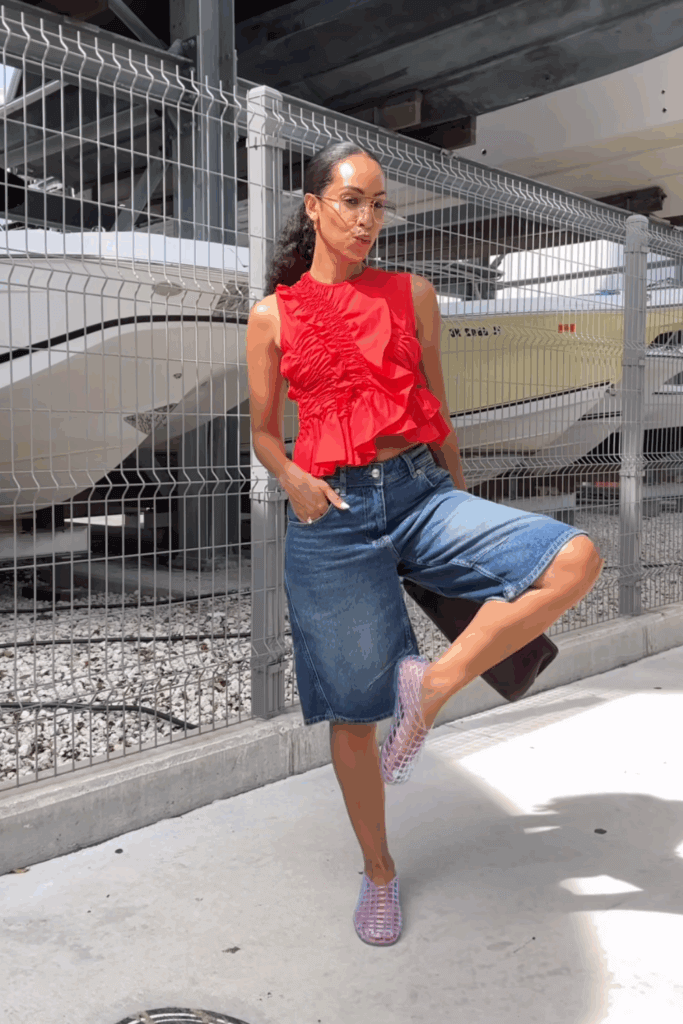 Young woman posing on street wearing trendy summer jelly shoes with a red ruffle top and jorts