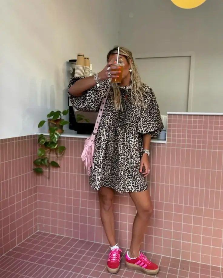 young woman wearing flowy leopard print mini dress with bold pink sneakers