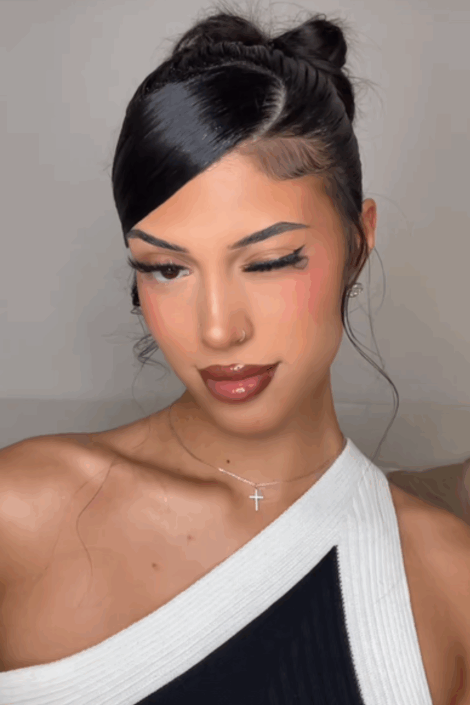 Young latina woman winking playfully at camera after she's done her date night hairstyle which is a slicked backed messy bun and dramatic side bang