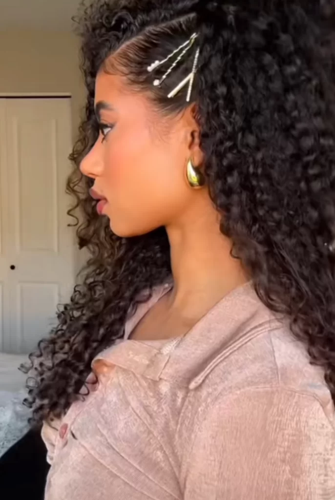 Young black woman and influencer showing her easy and effortless date night hairstyle where her natural curly hair is parted in the middle and a section clipped back behind her ear with decorative hair pins
