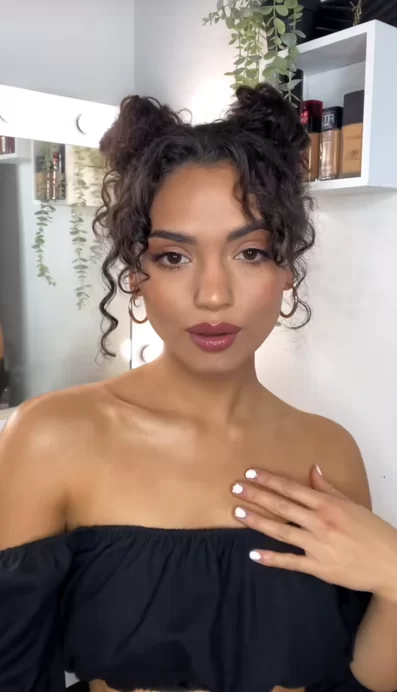 Space buns playful hairstyle shown on a woman with naturally dark curly hair