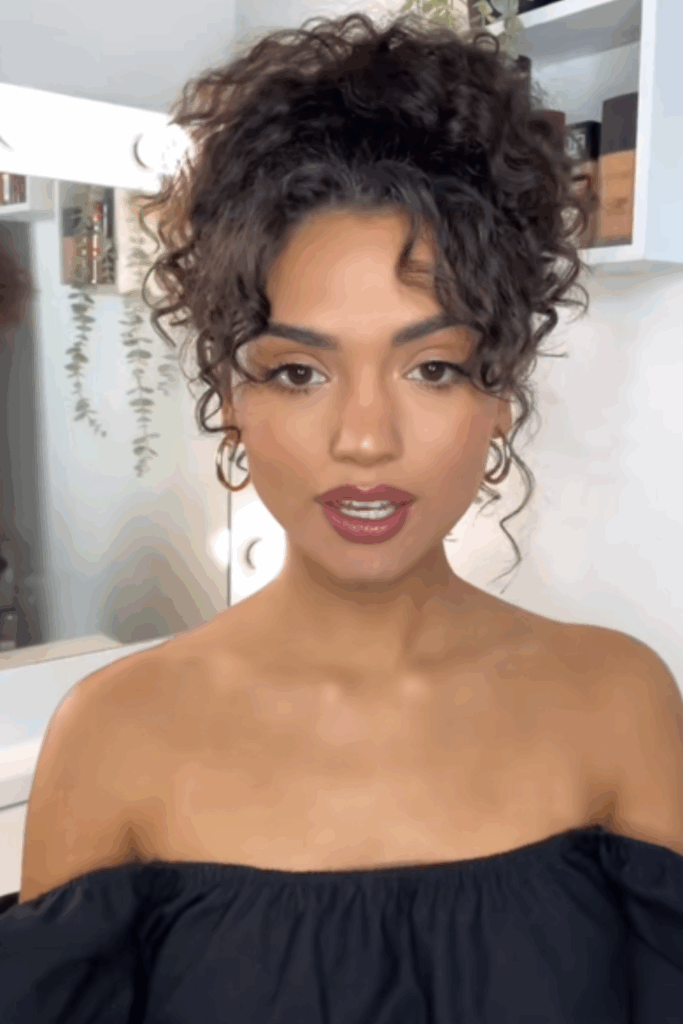 Young latina influencer showing off one of her go-to date night hairstyles where her naturally curly hair is easily pulled back onto her head into a bun with her smaller bangs pulled front